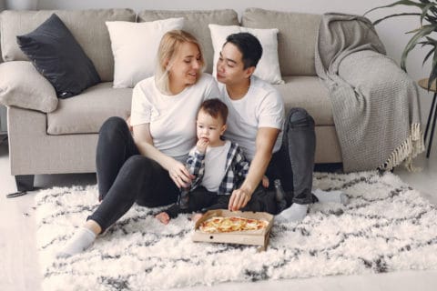 family sitting on a rug eating pizza
